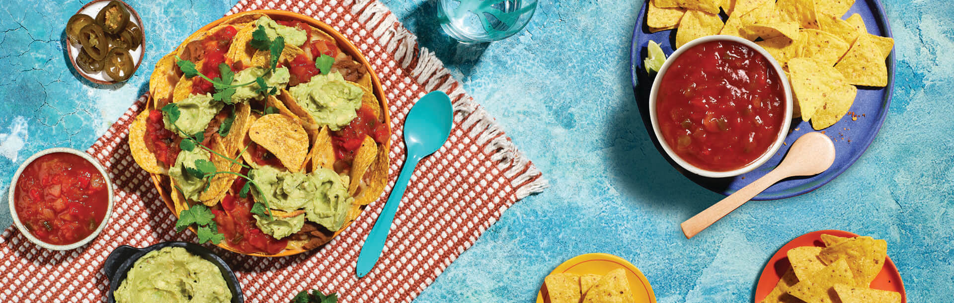 nachos serviti con guacamole e salsa in piatti su sfondo blu rustico